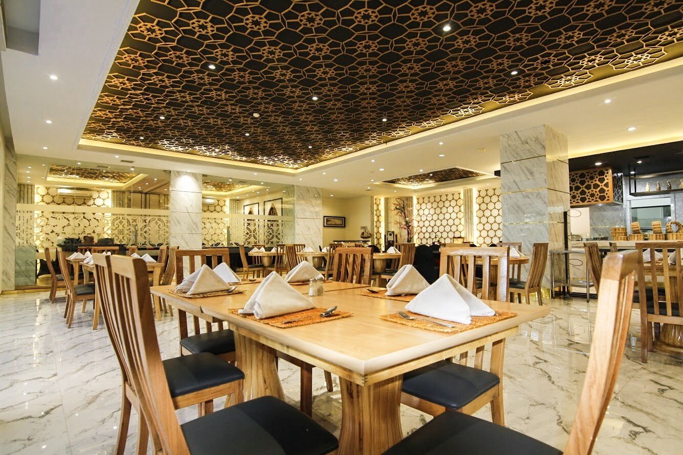 Un comedor amplio con mesas y sillas de madera, techo decorativo y piso de mármol.
