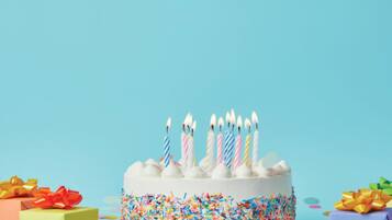 Un pastel de cumpleaños con velas, rodeado de confeti de colores y dos cajas de regalo.
