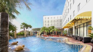 Ein Hallenbad mit Blick auf ein Hotelgebäude, Palmen und Außenbereiche mit Sitzgelegenheiten.