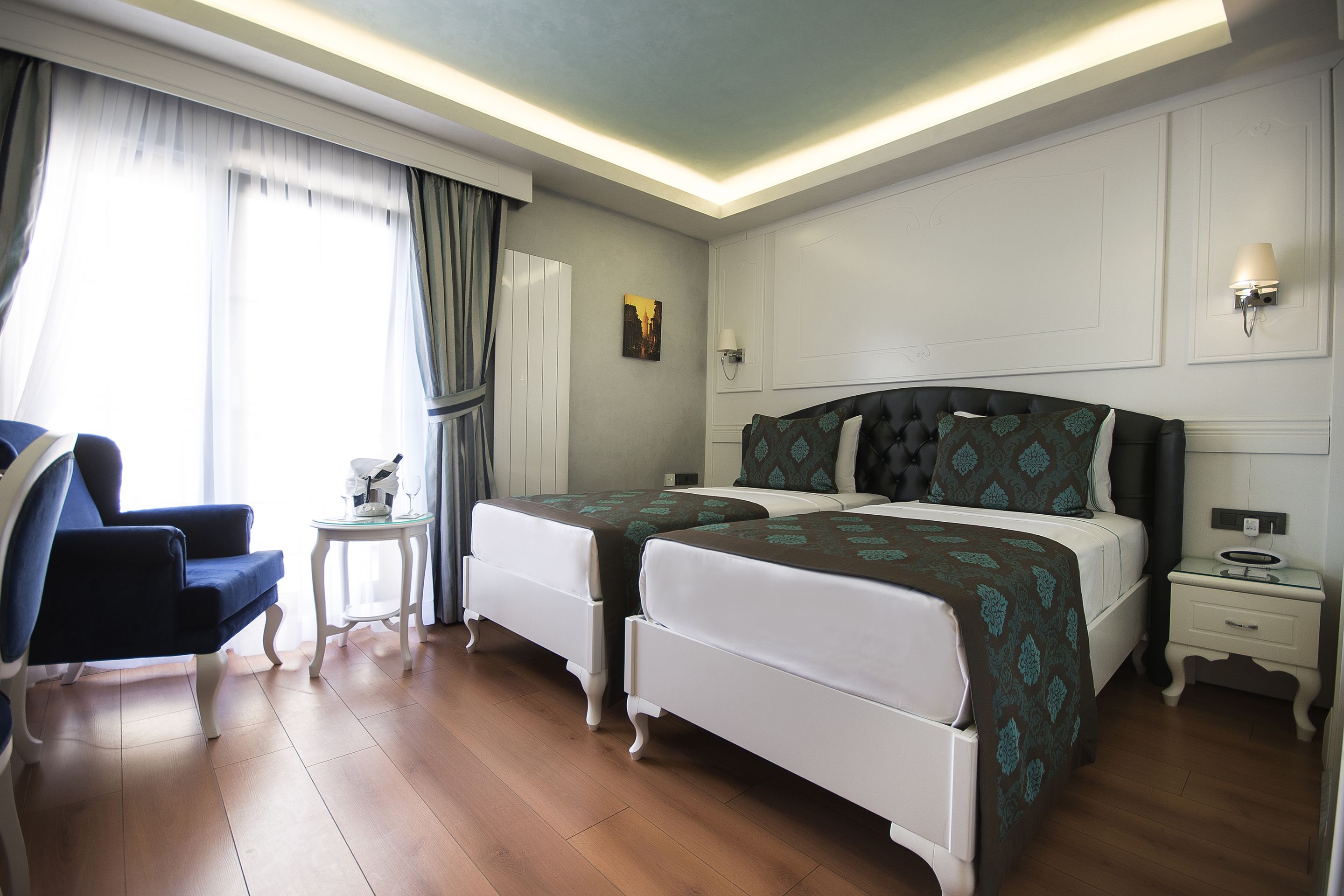 A hotel room with two single beds, a chair, a small table, and a nightstand.
