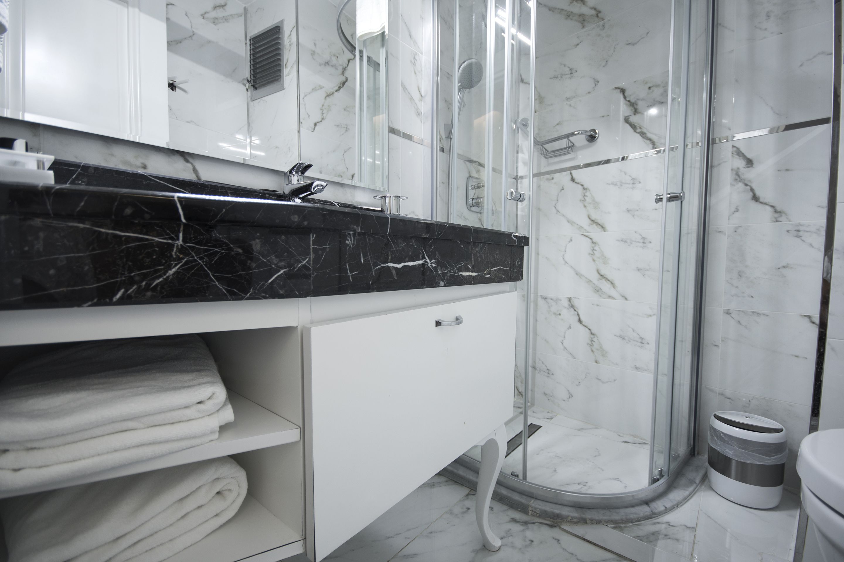 Une salle de bain moderne avec un lavabo en marbre, une douche en verre et des serviettes soigneusement pliées.