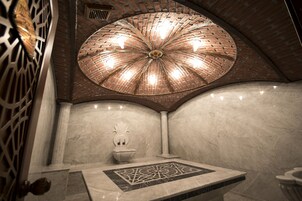 Un baño con piso de baldosas, pared de mármol, lavamanos blanco decorativo e iluminación circular en el techo.