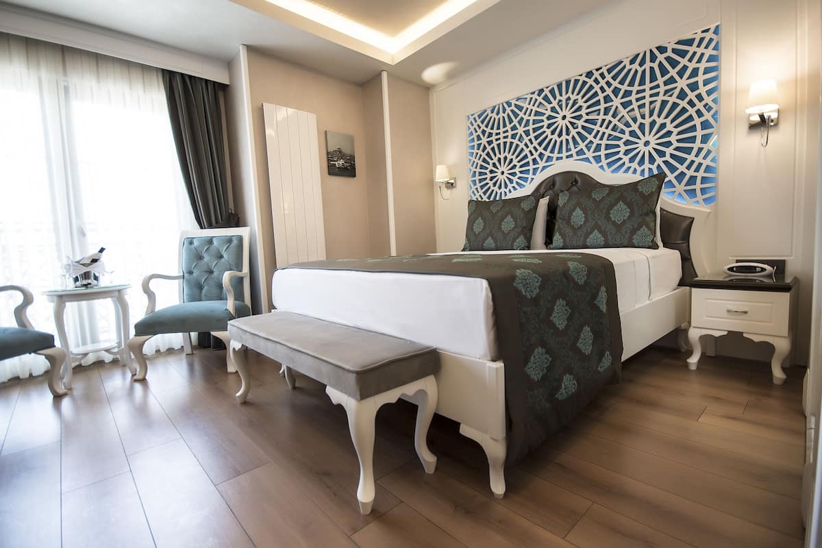 Ein Hotelzimmer mit Bett, Nachttisch, Stuhl, Bank und einer Wand mit Dekor.