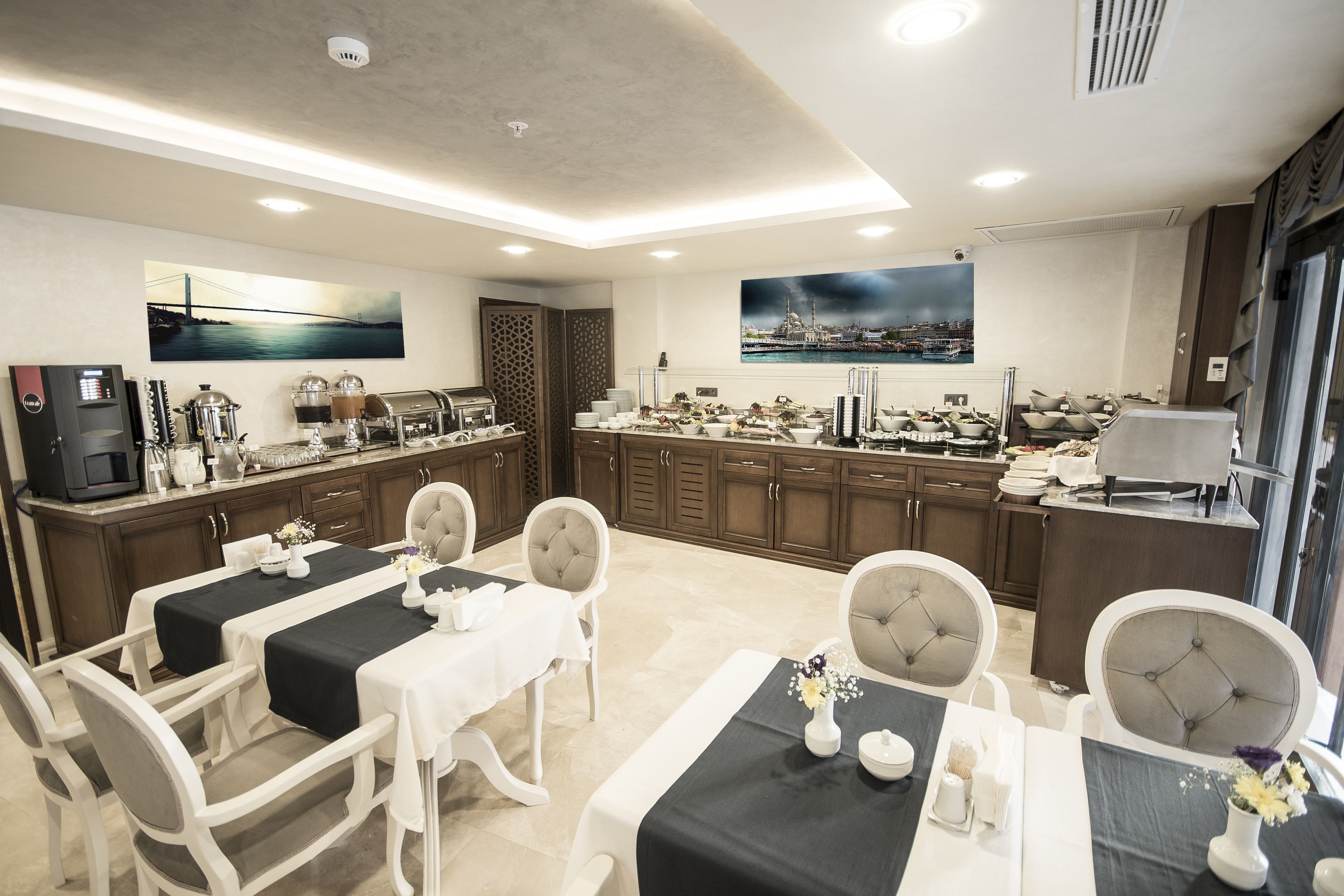A modern dining area with a long table, white chairs, and a kitchen in the background.