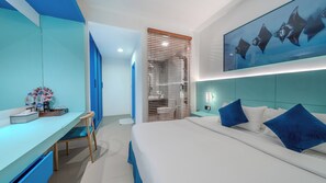 A modern hotel room with a bed, a desk, and a bathroom visible through a glass partition. - LVIS blancura (Dharavandhoo)