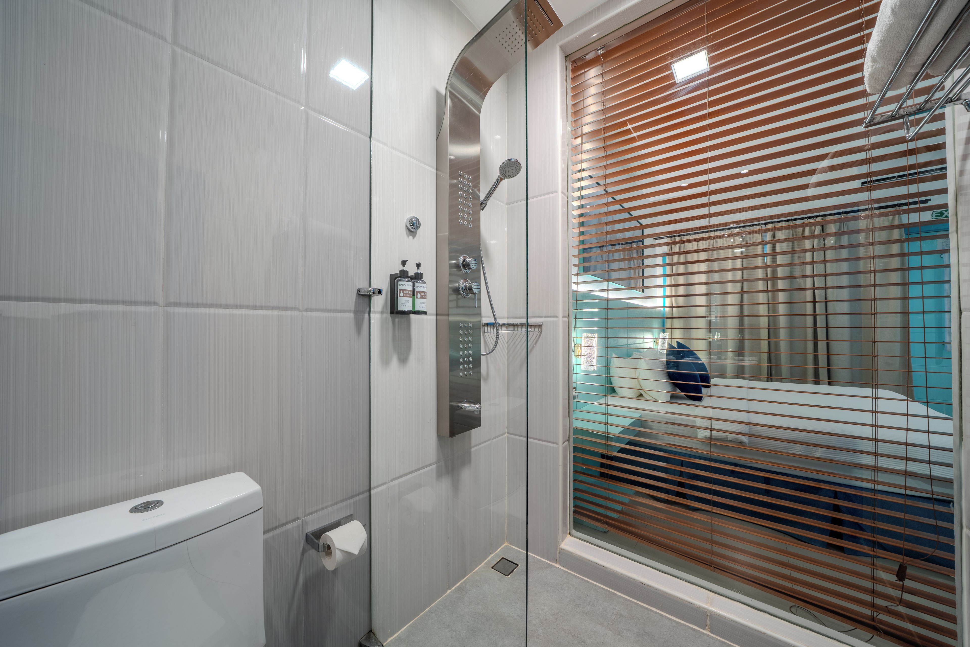 Un baño moderno con cabina de ducha de vidrio, inodoro y ventana con persianas.