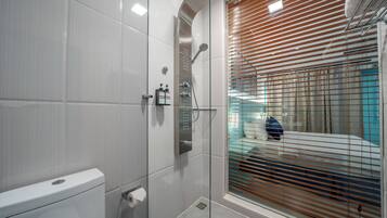 Un baño moderno con cabina de ducha de vidrio, inodoro y ventana con persianas.
