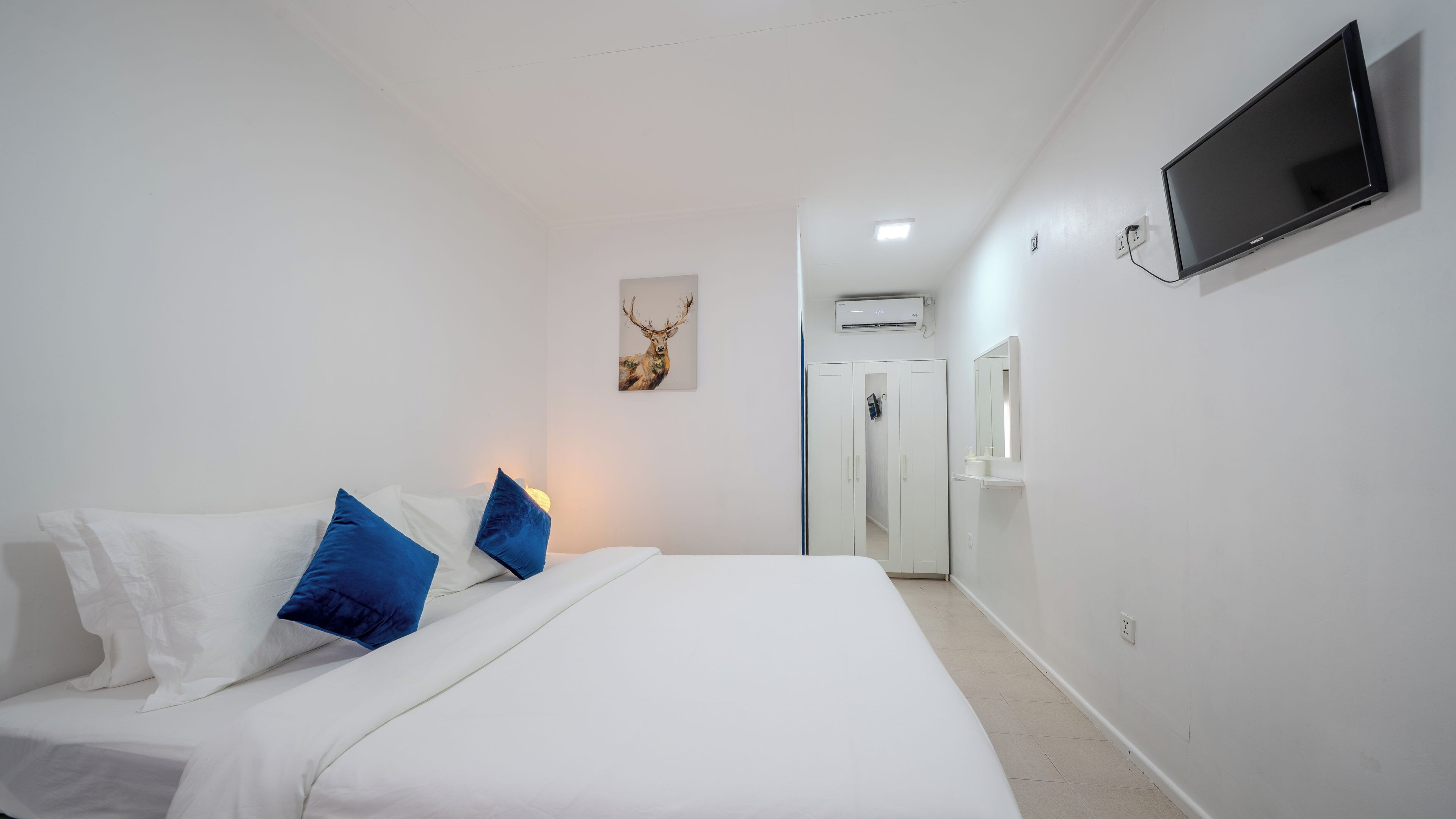 A hotel room with a bed, a mounted TV, a wall-mounted mirror, and a door leading to a bathroom.