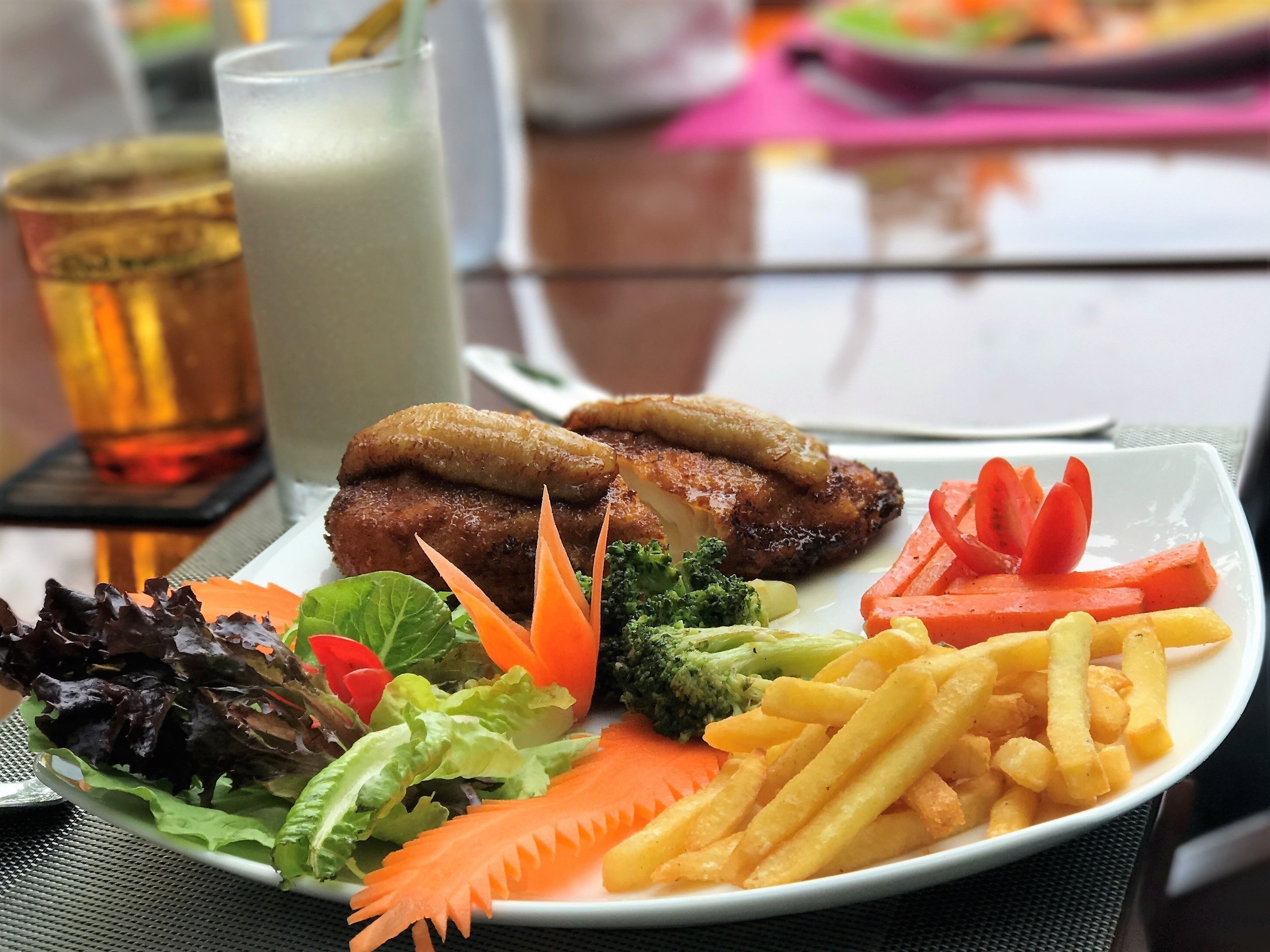 A plate of food including a meat patty, fries, vegetables, and a drink.