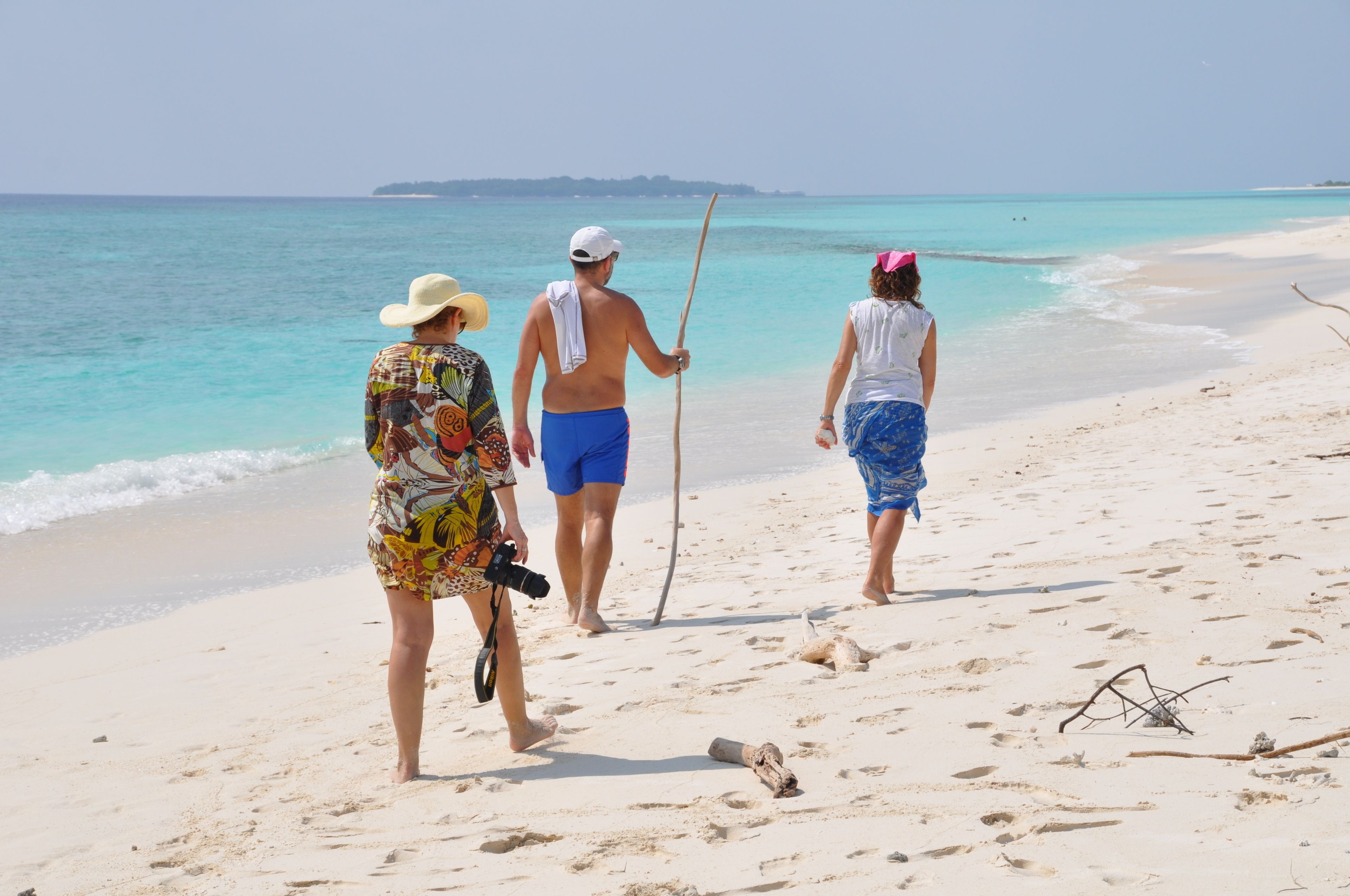 Three people walking on a sandy beach with a clear view of the ocean and distant land.
