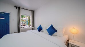 Habitación de hotel con cama, escritorio, silla, lámpara, ventana con cortinas y puerta con letrero de no fumar.
