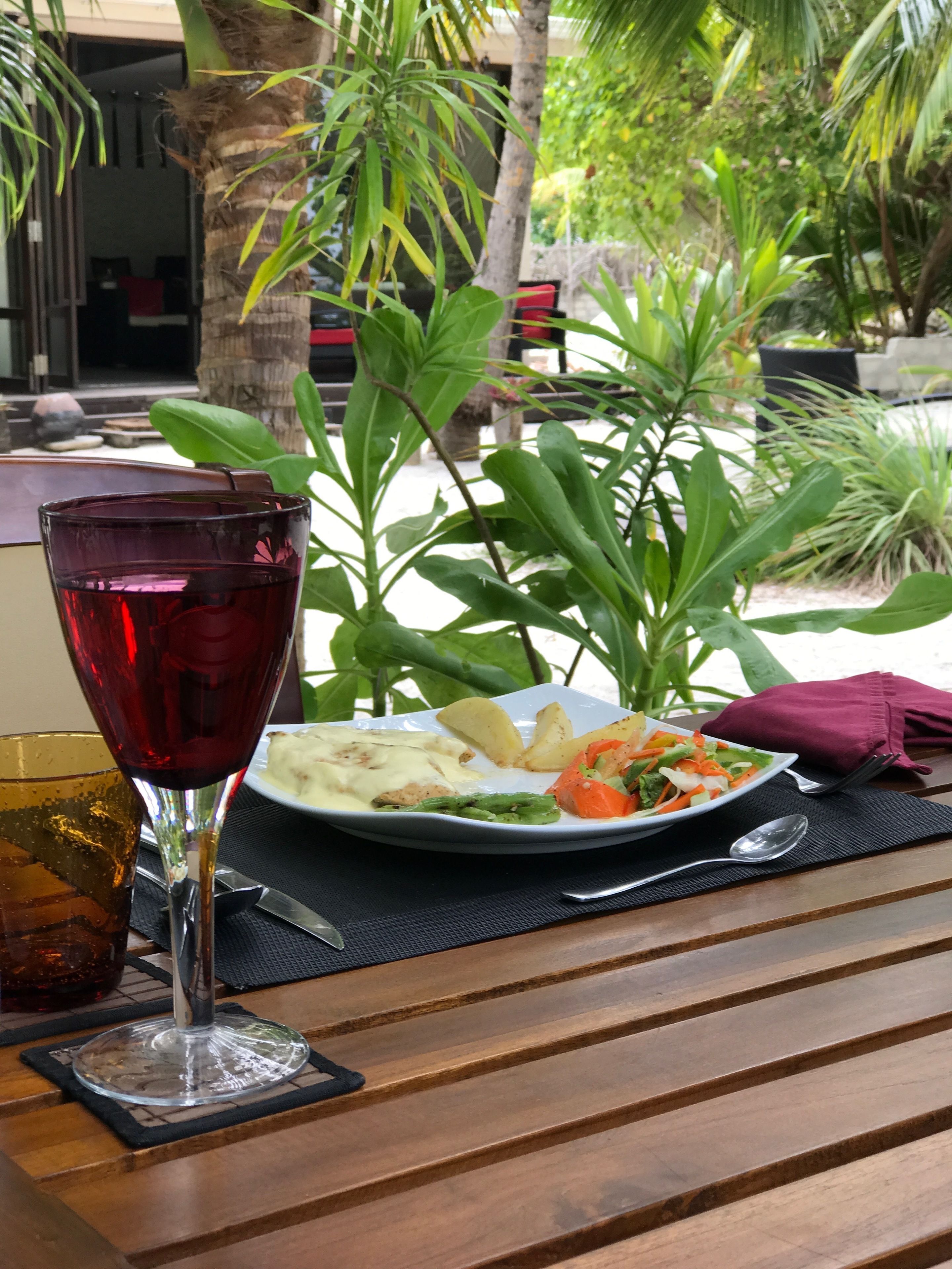 A table with a plate of food, a glass of red wine, and a spoon.