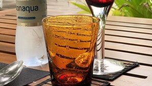 A bottle of Bonagua water, a red wine glass, and a yellow glass with a spoon on a wooden table outdoors. - LVIS blancura (Dharavandhoo)