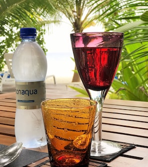 A bottle of Bonagua water, a red wine glass, and a yellow glass with a spoon on a wooden table outdoors. - LVIS blancura (Dharavandhoo)