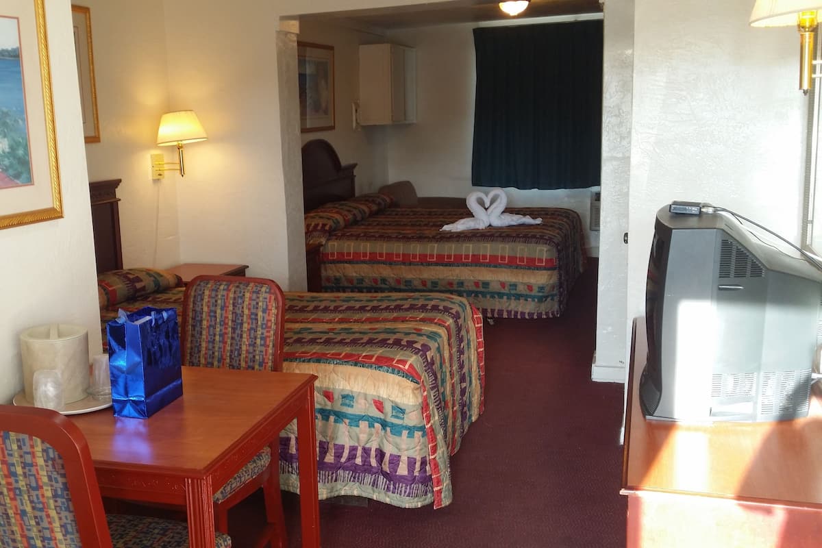 A hotel room with two beds, a desk, a chair, a television, and a painting on the wall.