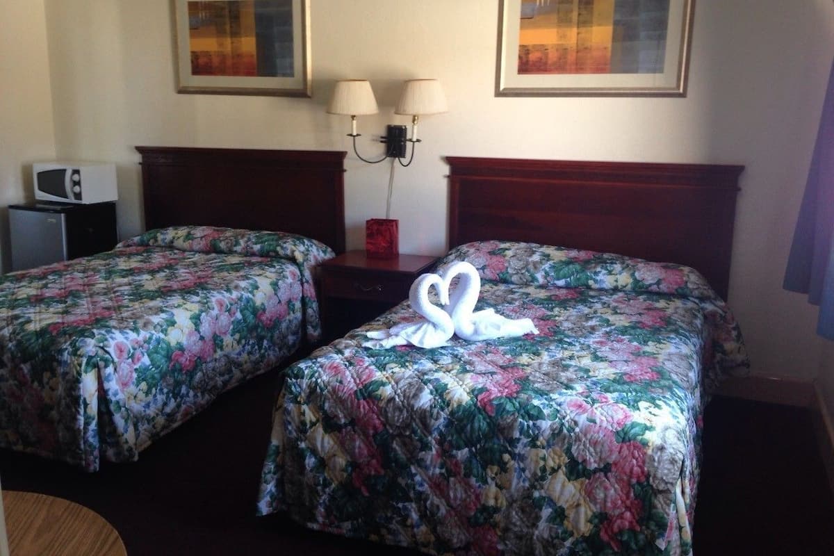 A hotel room with two single beds, a nightstand, a lamp, and a microwave.