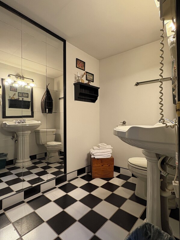 A bathroom with a black and white checkered floor, a white sink, a toilet, and a mirror with lights. - Whiteface Farm Adirondack Bed and Breakfast (Wilmington)