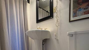 A bathroom with a white sink, a toilet, a shower curtain, and a framed painting on the wall.