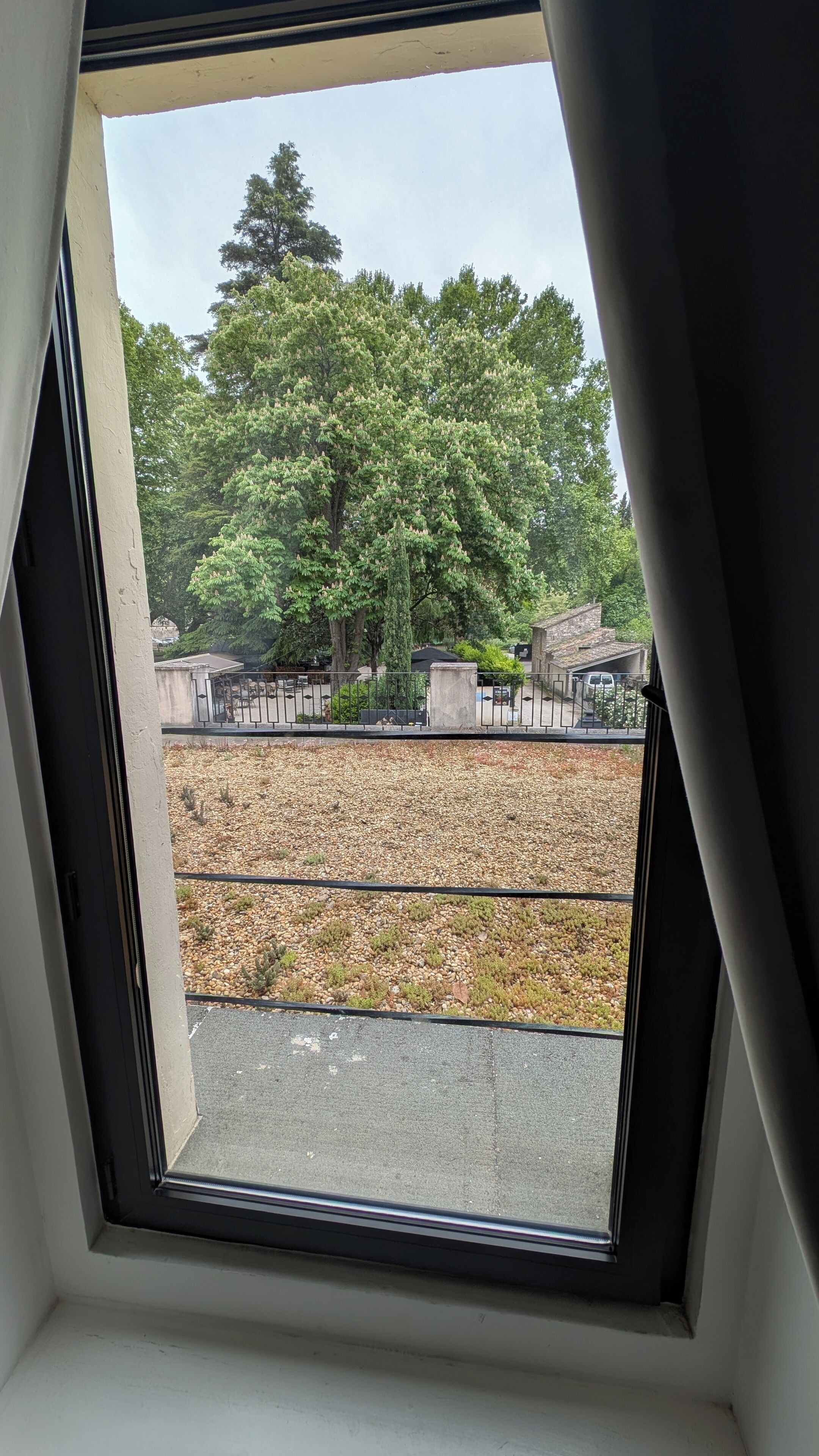 Une fenêtre donnant sur un cimetière, des arbres et un chemin de gravier.