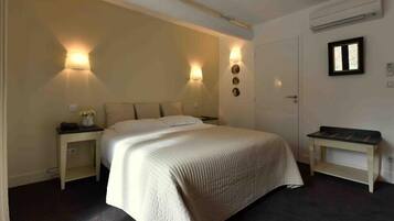 Ein Hotelzimmer mit Bett, Nachttischen, Wandlampen, einer Tür und einer kleinen Bank.