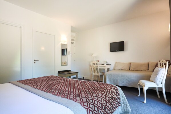 Een hotelkamer met een bed, een bureau, een stoel, een bank en een televisie aan de muur.