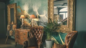 Una habitación con un sillón de cuero marrón, una lámpara blanca, un espejo grande y una planta en maceta.