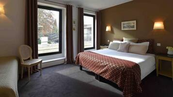 Habitació d'hotel amb un llit gran, una cadira, una tauleta de nit i una finestra amb cortines.