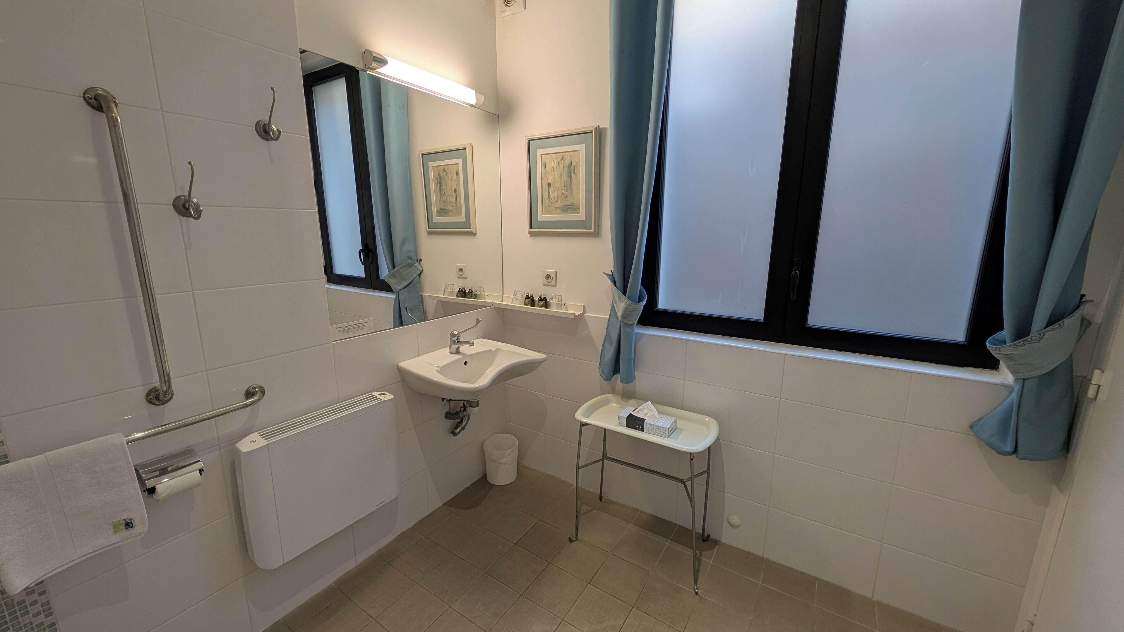 A bathroom with a white sink, a mirror, a toilet, a hand dryer, and a window with curtains.