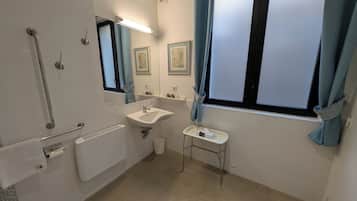 A bathroom with a white sink, a mirror, a toilet, a hand dryer, and a window with curtains.