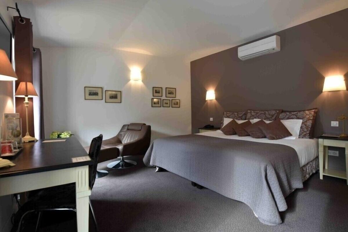 Una habitación de hotel con una cama, un escritorio, una silla y lámparas fijadas a la pared.