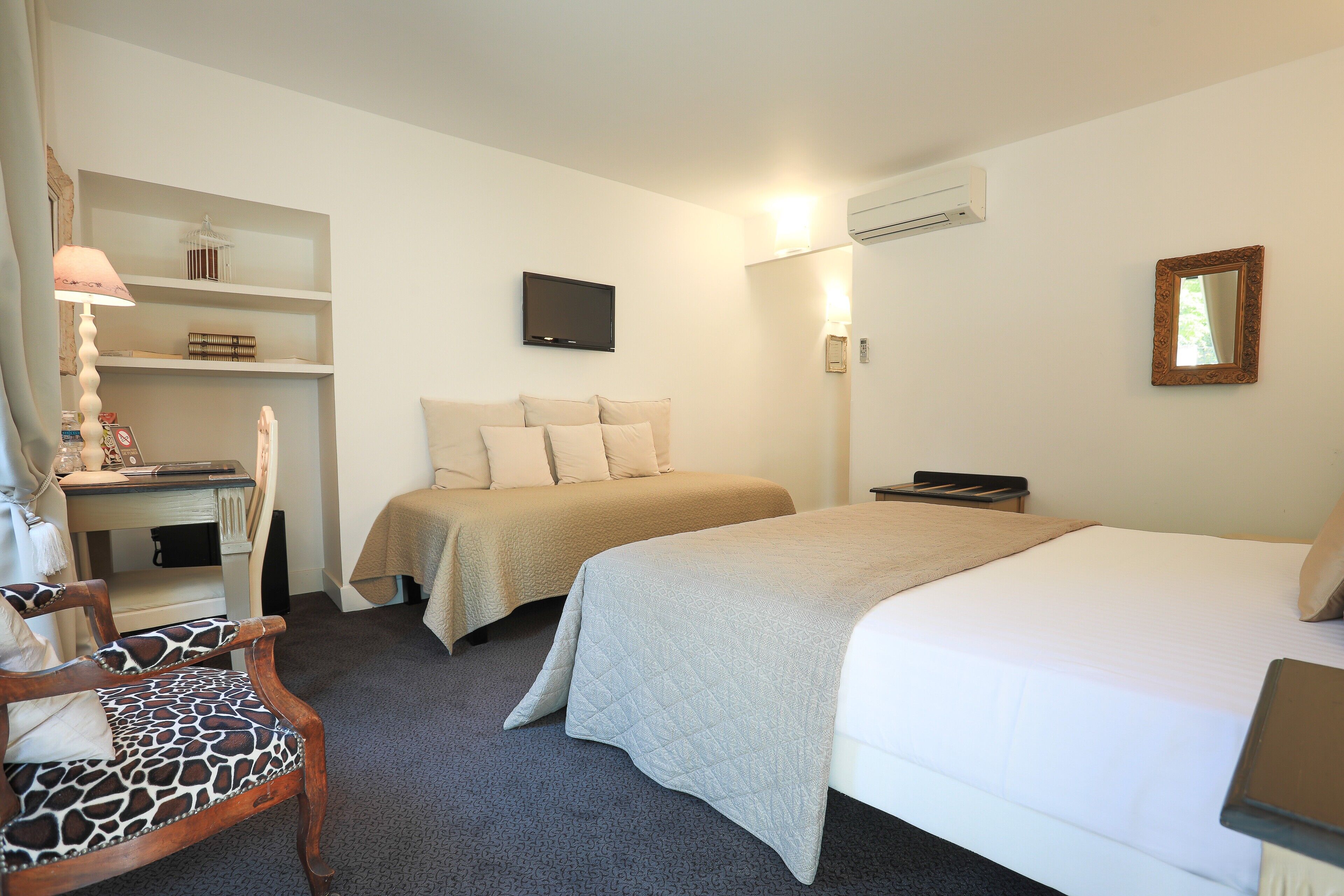 A hotel room with a bed, a desk with a chair, a TV, and a bookshelf.