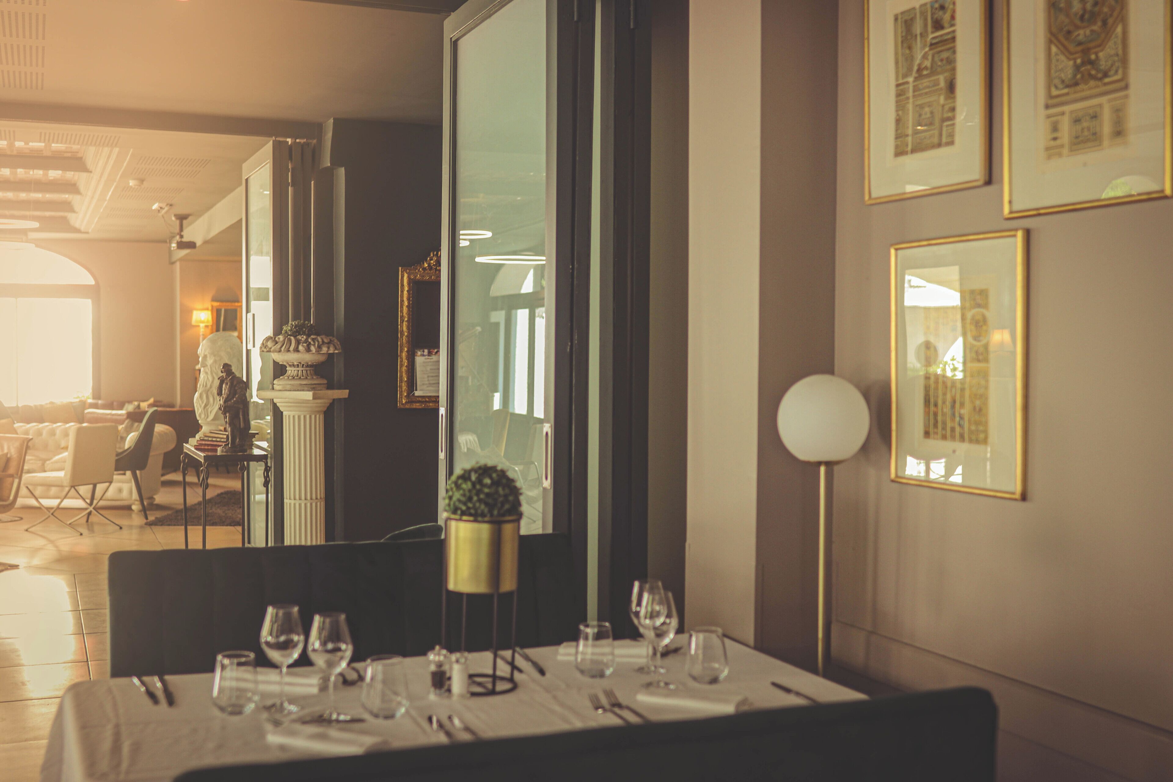 A dining area with a table set for a meal, a potted plant, and framed artwork on the walls.