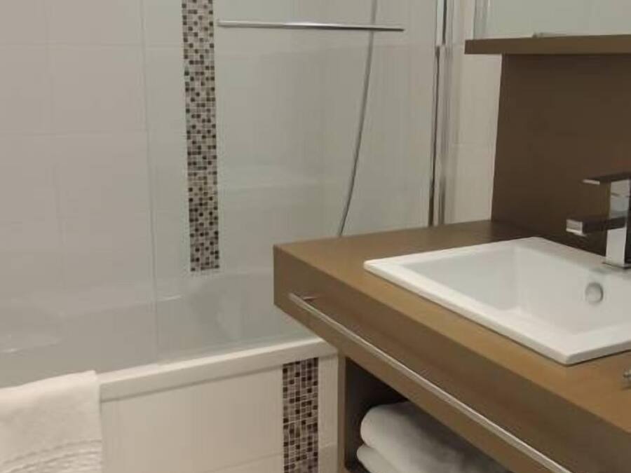 A modern bathroom with a glass shower enclosure, a white bathtub, and a wooden vanity with a white sink.