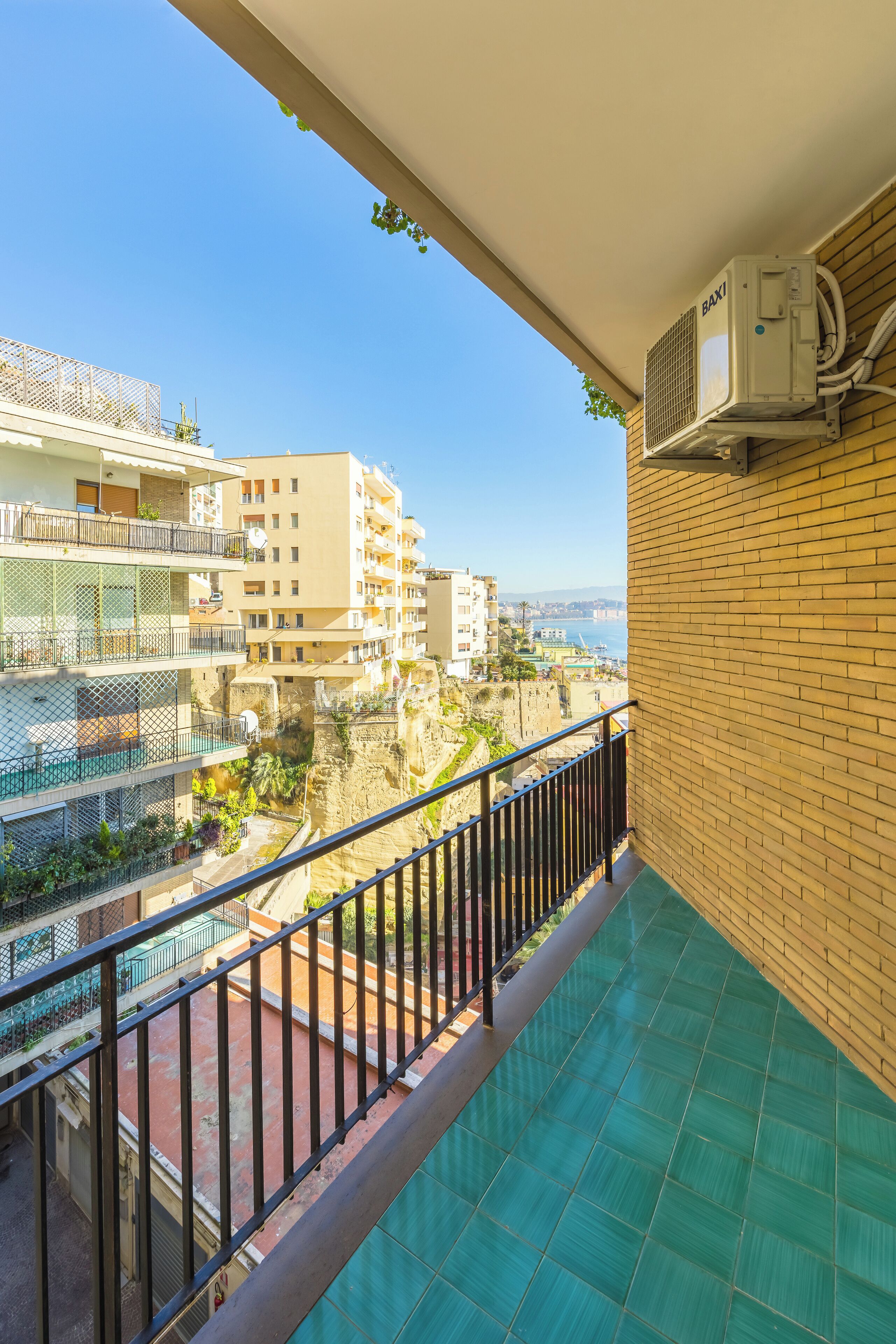 A balcony with a view of a coastal area, featuring a brick wall and a metal railing.