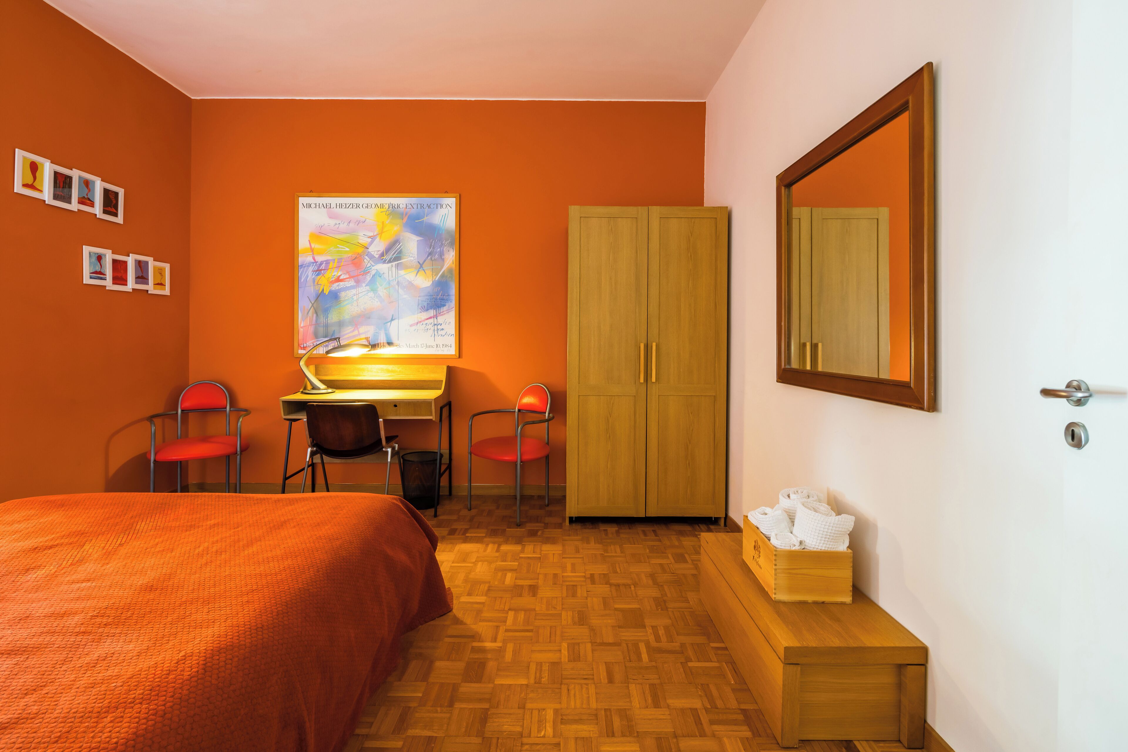 A hotel room with a bed, a desk, two chairs, a wardrobe, and a mirror.