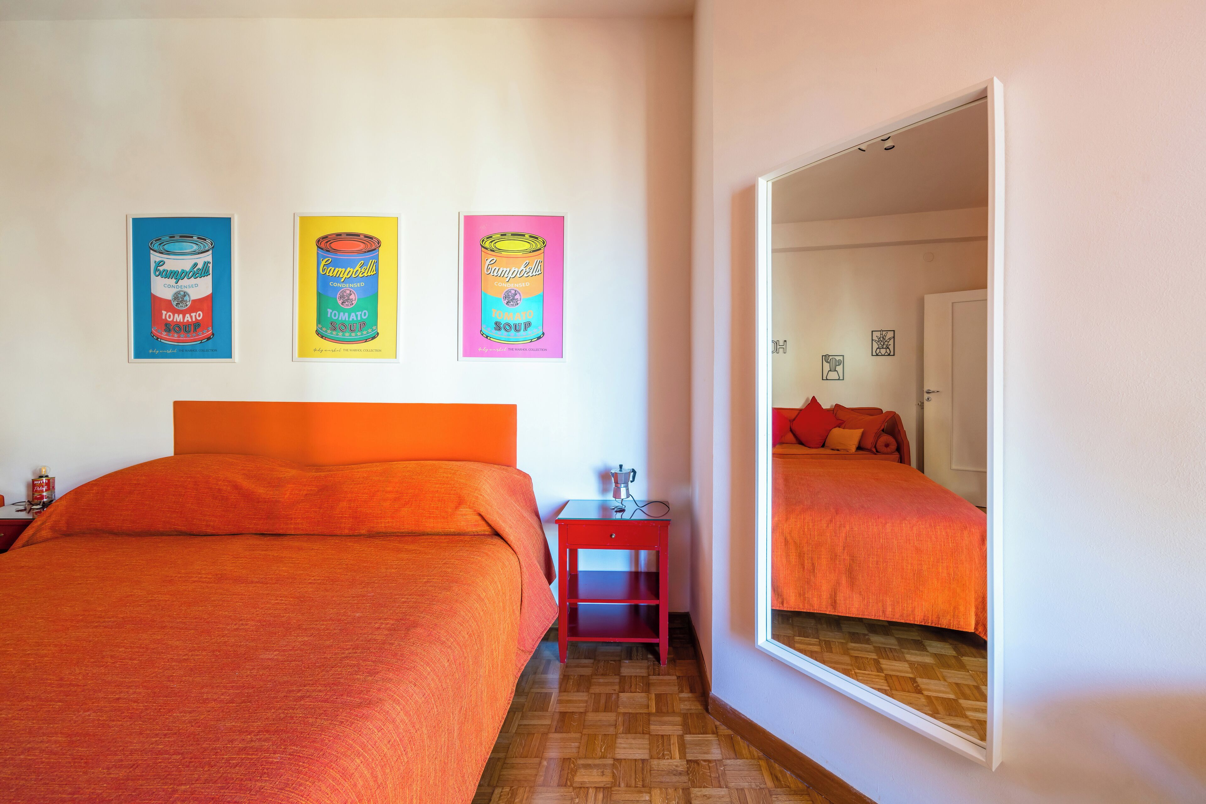 A hotel room with two beds, a red nightstand, and three colorful Campbell's soup can posters on the wall.
