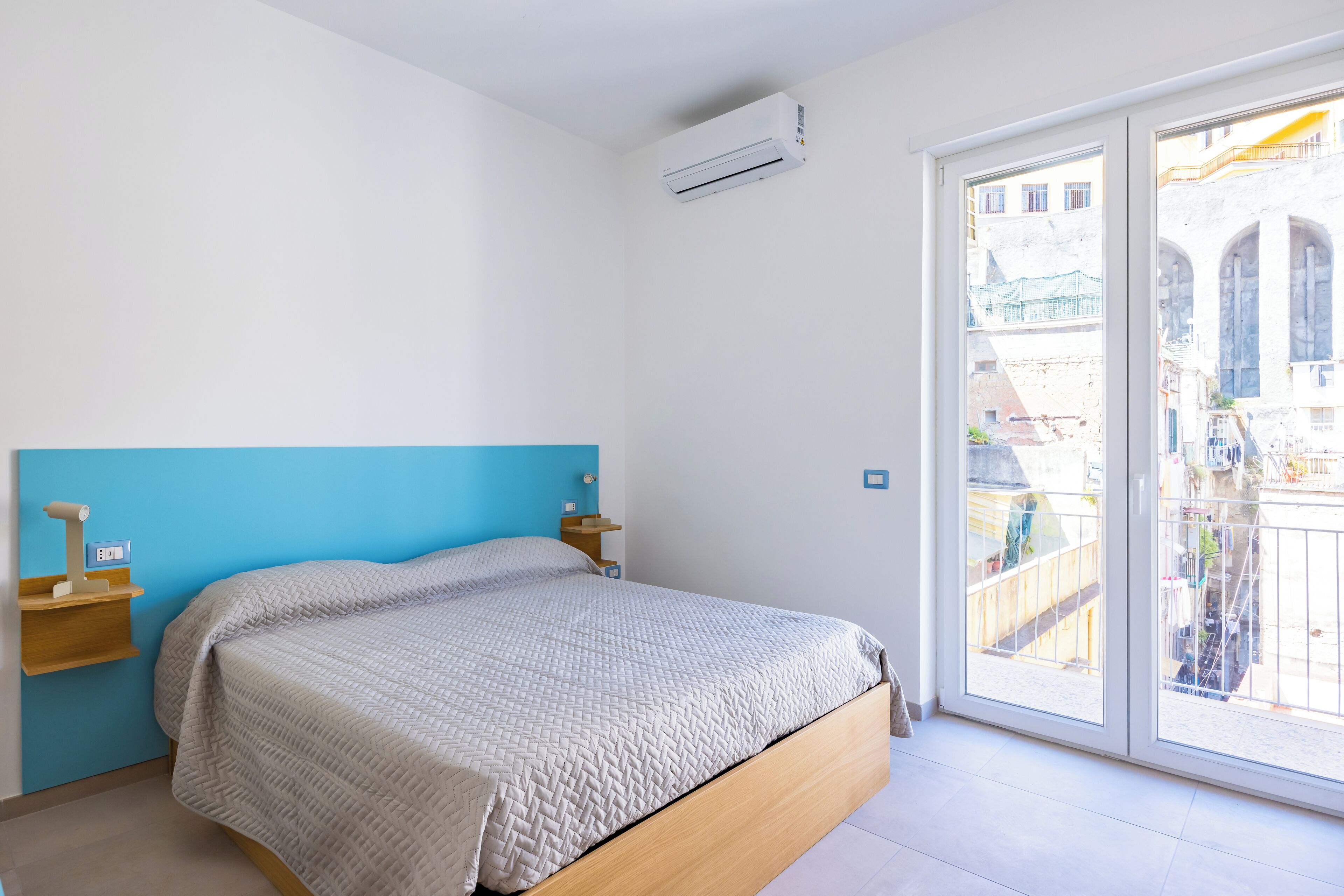 Ein Schlafzimmer mit Bett, blauer Wand, Fenster und Klimaanlage.