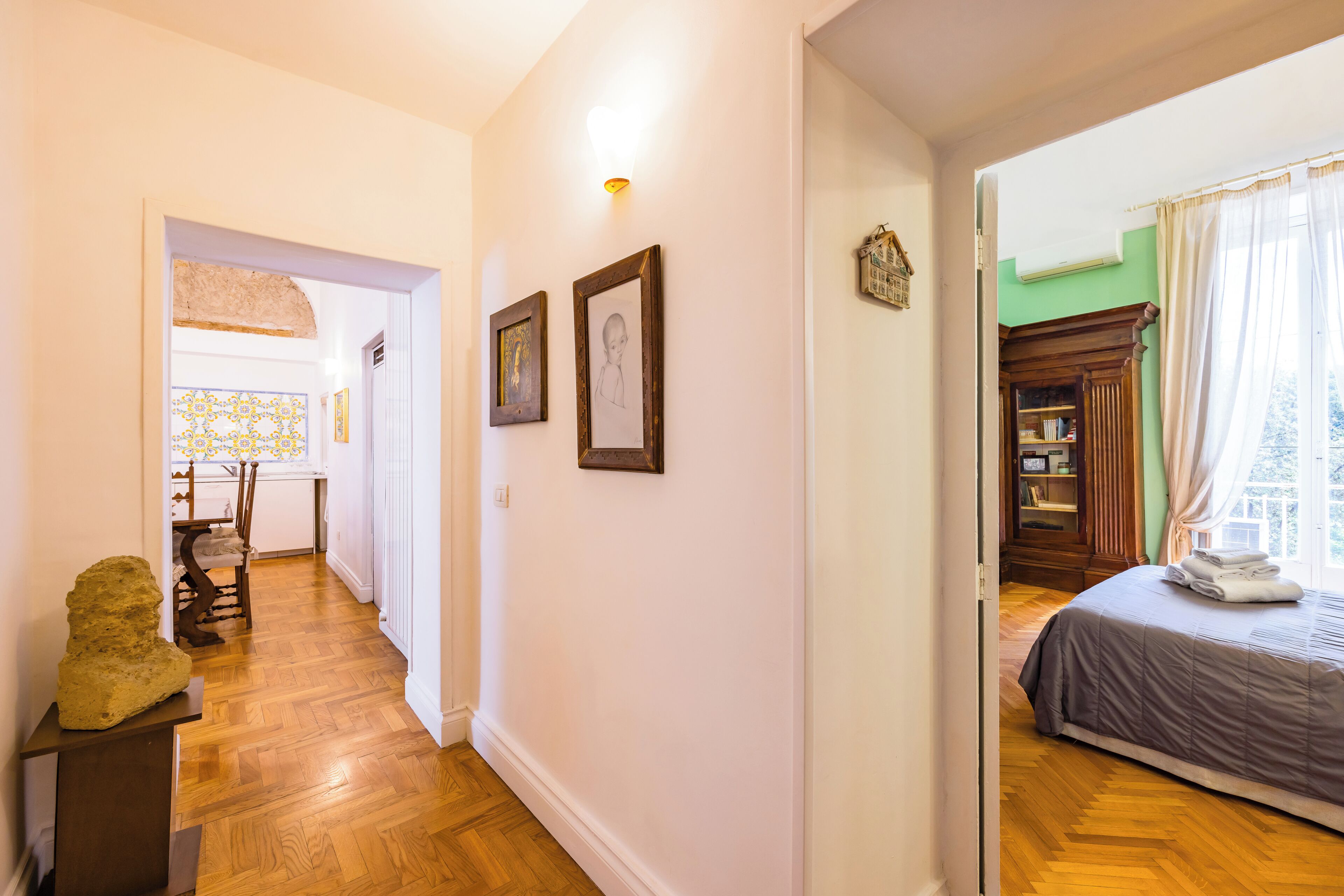 Un pasillo con piso de madera que conduce a un dormitorio con cama y ventana.