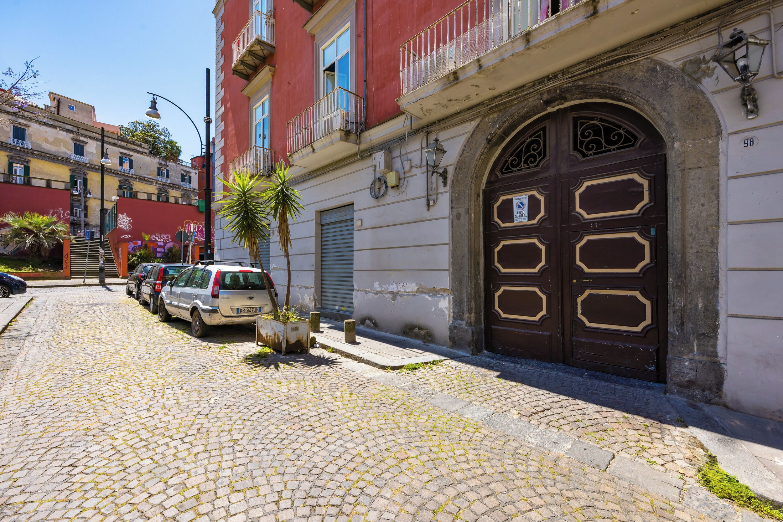 A cobblestone street with parked cars and a building with a large, ornate door.