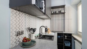 A modern kitchen with a grey countertop, a built-in oven, and a microwave. There are two shelves above the counter holding kitchenware. - ShortStayPoland Marszałkowska B188 (Warsaw)