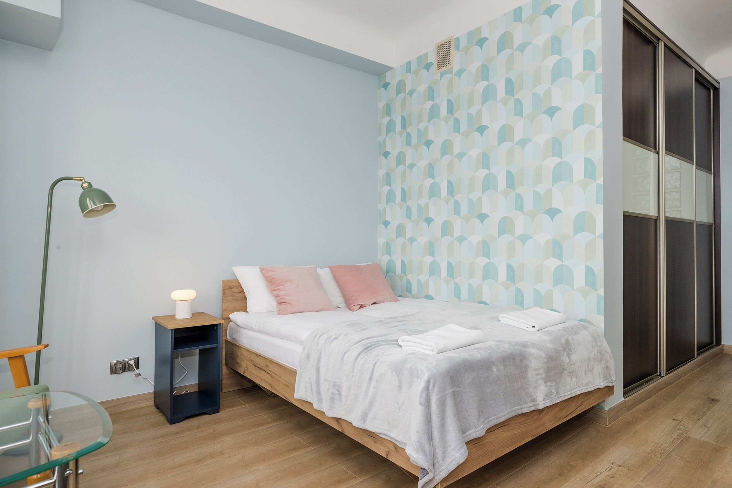 Un dormitorio con cama, mesita de noche, lámpara y pared decorada.