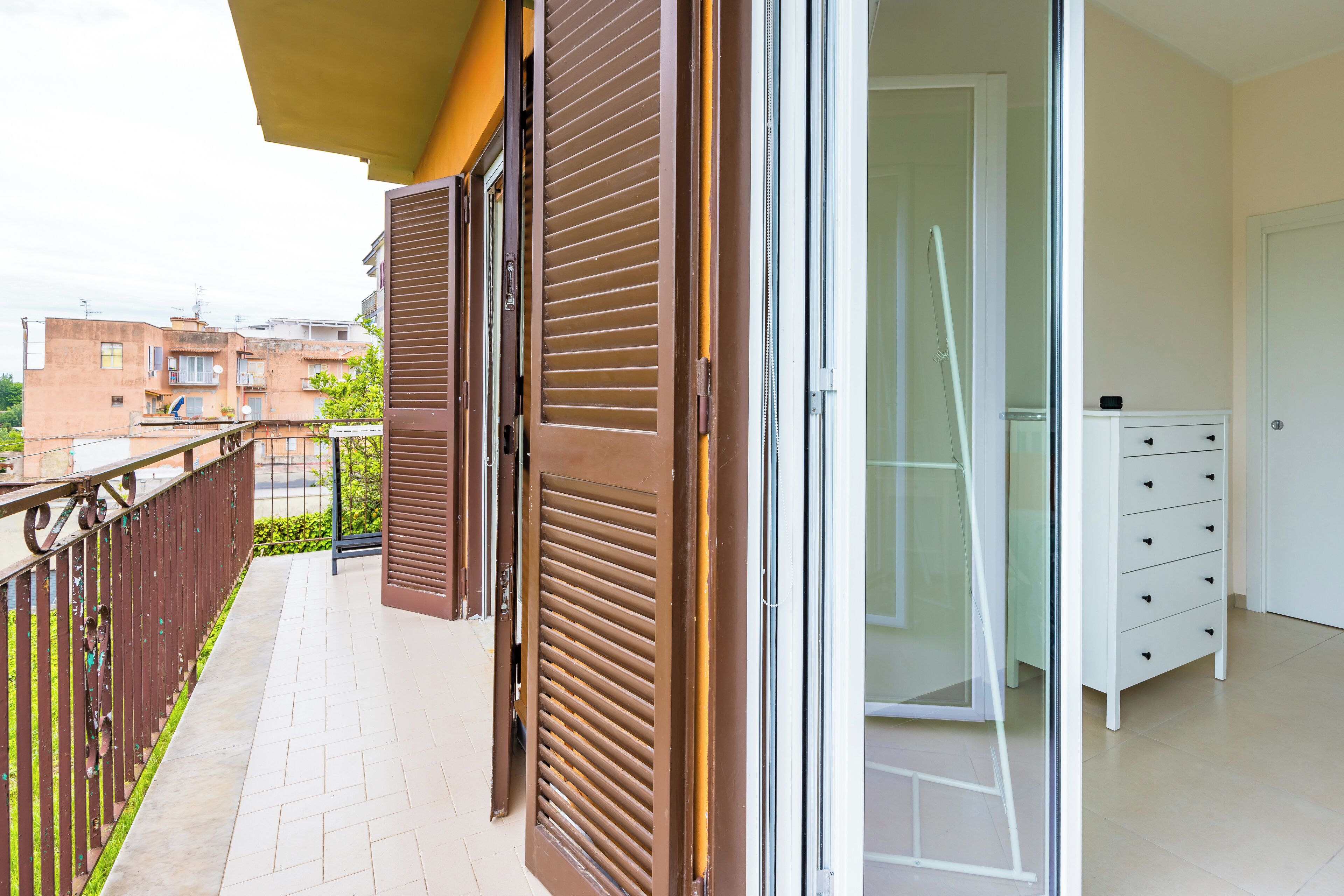 A balcony with brown shutters, a glass door, and a white dresser.