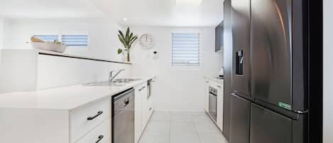 Una cocina moderna con armarios blancos, electrodomésticos de acero inoxidable y un refrigerador negro.