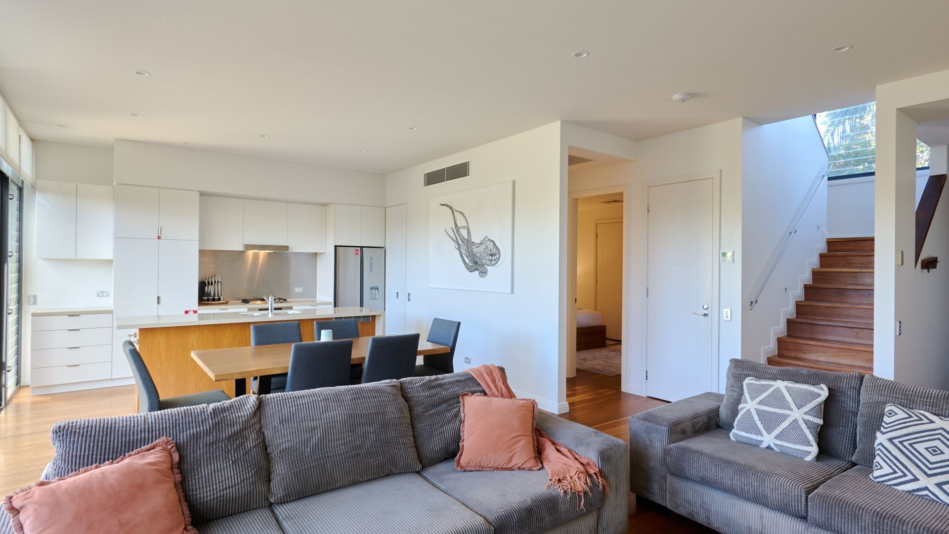 A modern living space with a kitchen, dining area, and two sofas with cushions.