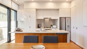 A modern kitchen with white cabinets, a stainless steel refrigerator, and a central island with chairs.