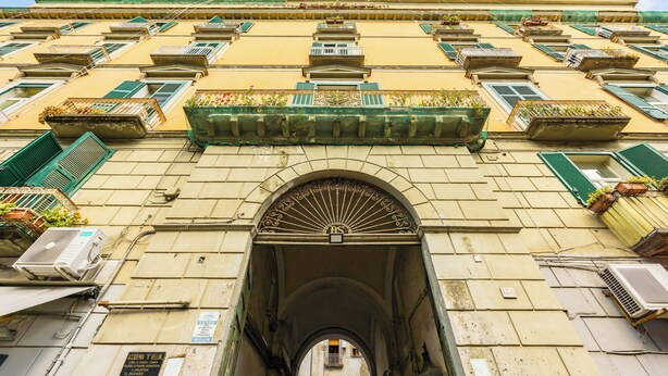 A building with multiple balconies, an archway entrance, and air conditioning units. - Guest Rooms Bellini  (Naples)