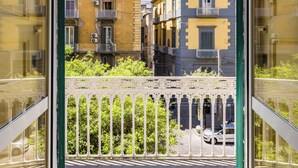 A view from a balcony with a railing, overlooking a street with buildings and a parked car. - Guest Rooms Bellini  (Naples)