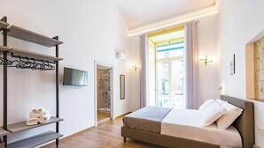 A modern hotel room with a bed, a coat rack, a flat-screen TV, and a view of the outside. - Guest Rooms Bellini  (Naples)