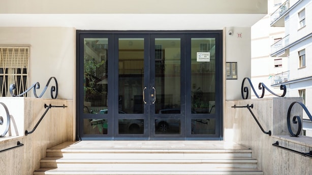 A building entrance with a glass door, metal railings, and a staircase leading up. - Fresh and Trendy Flat at Vomero (Naples)