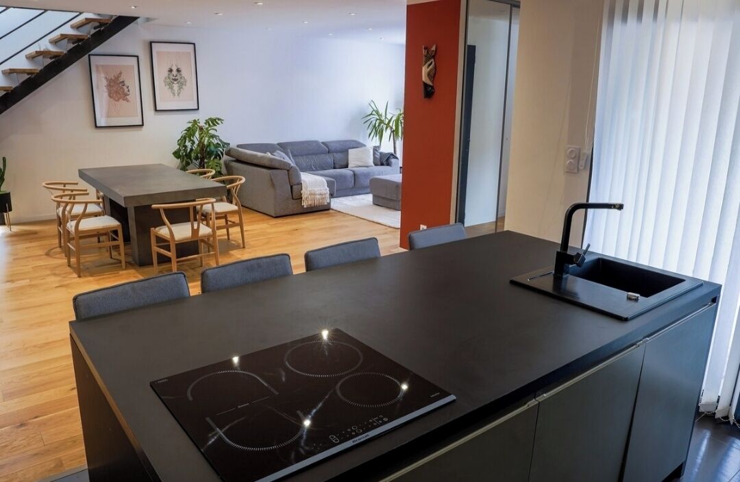 Een moderne keuken met een centraal eiland, een eethoek met tafel en stoelen, en een zithoek met een bank en planten.